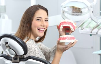 Young Woman in Dentist Chair Holding Model of Teeth Philadelphia PA